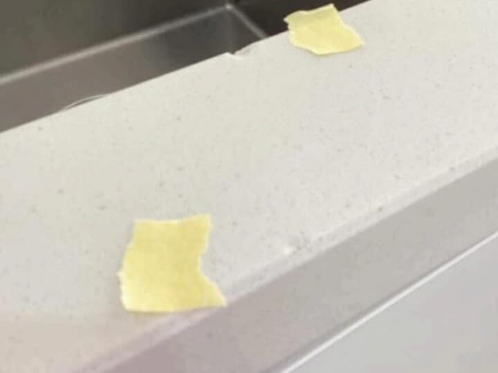 Before: a chip on the edge of a white engineered stone benchtop next to a stainless steel sink.